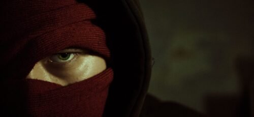 Close-up of a person with a red mask revealing only an eye, conveying mystery.